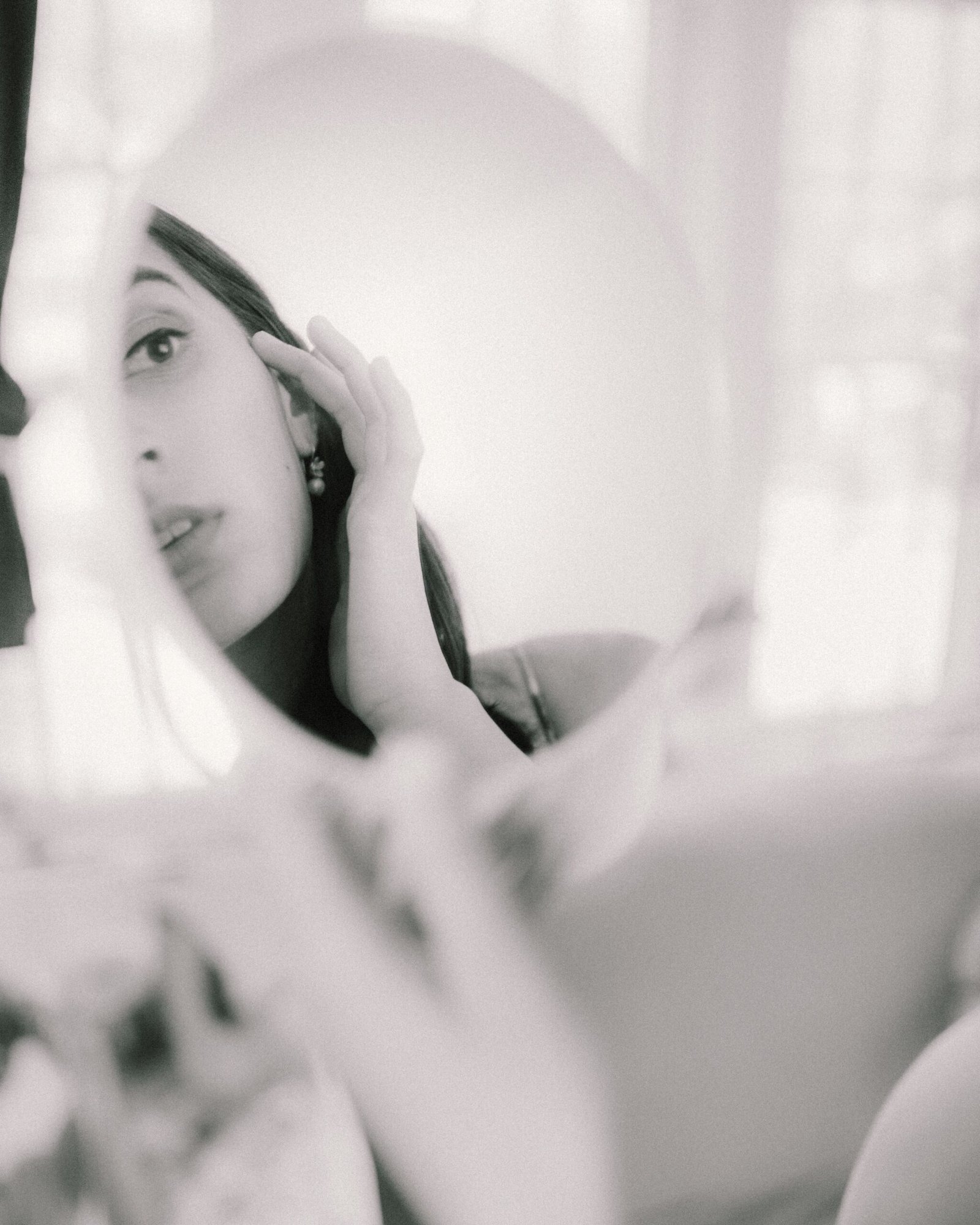 Elegant black and white photo of a woman gazing at her reflection in a mirror.